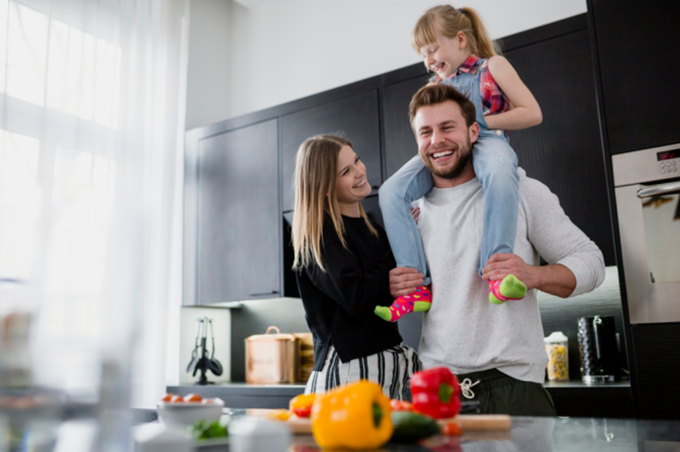 mom dad and daughter having fun in the kitchen with cabinets in background and red and yellow bell peppers on kitchen island in foreground